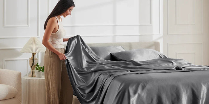 A person making a bed with smooth gray sheets