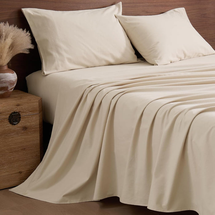 Cream-colored bed sheets with a smooth drape and matching pillowcases on a bed with a wooden headboard.