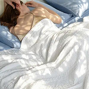 Woman sleeping comfortably under a white Bedelite waffle weave blanket with light blue bed sheets and pillows